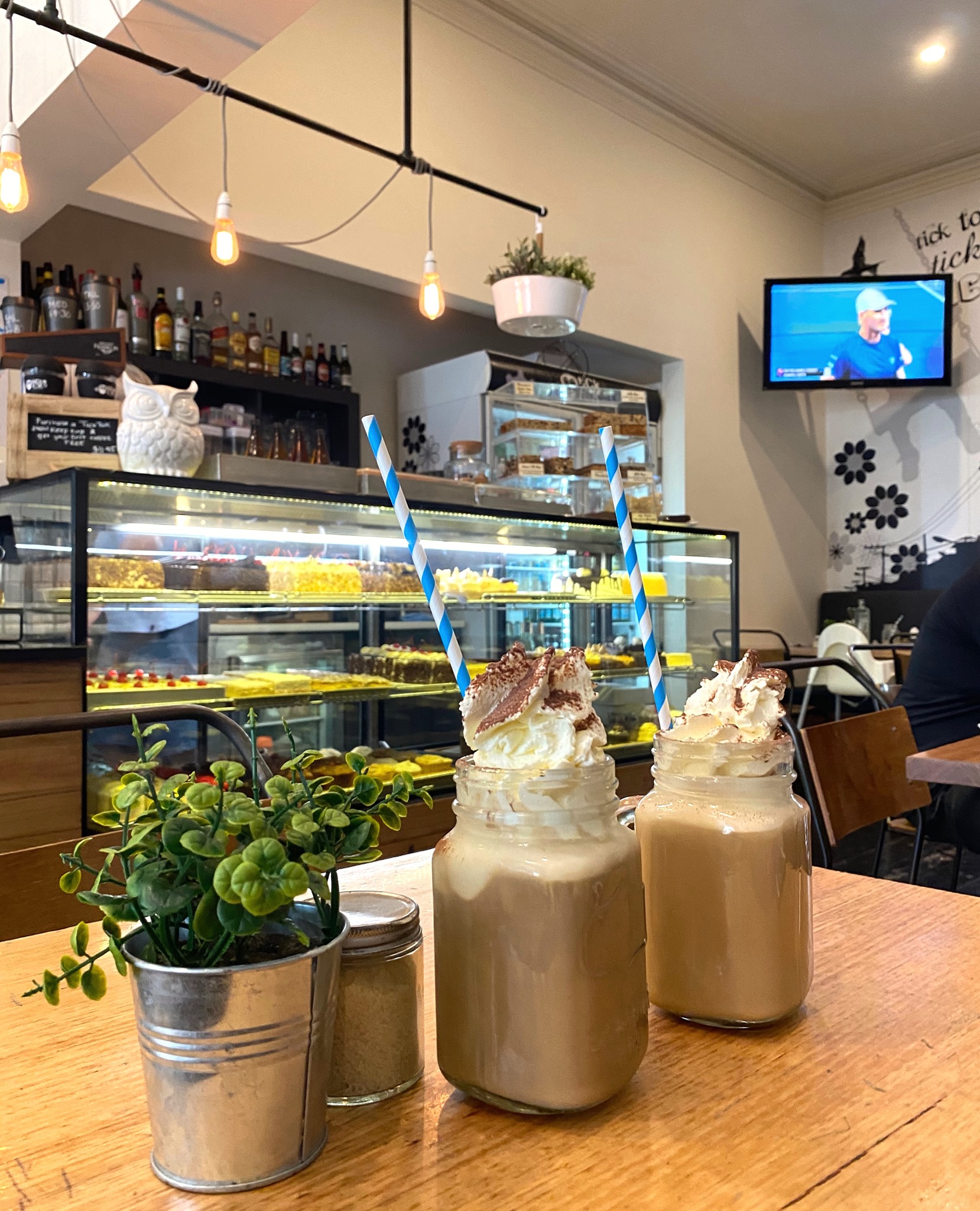 Indoor cafe counter with patisserie display case, espresso bar and milkshakes on a wooden table